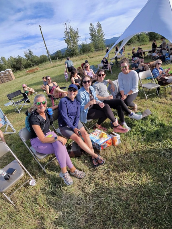 Board members seated in chairs on a grassy hillside at an outdoor event, smiling at the camera with a large tent structure visible behind them