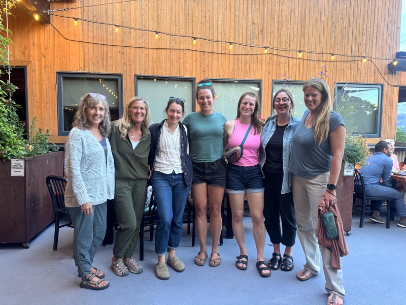 The GEA Alliance board and Angie gathered for a group photo under string lights on a wooden patio at Thursday's welcome dinner in Hood River